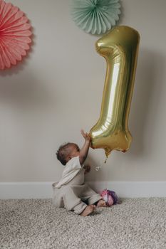 Cute baby with a golden balloon, celebrating a first birthday indoors.