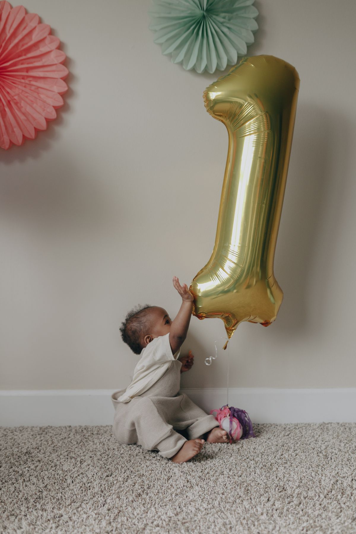 Cute baby with a golden balloon, celebrating a first birthday indoors. Stock Photo.
