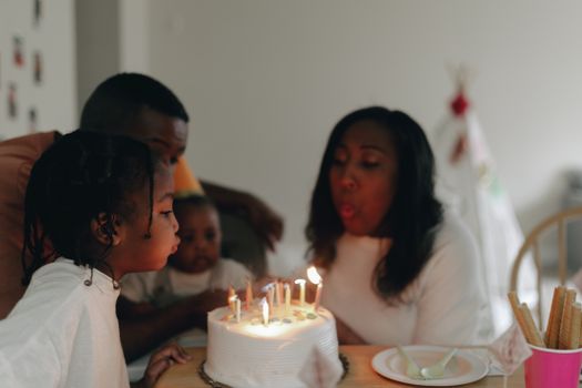 A joyful family celebrating a birthday by blowing out candles on a cake indoors.