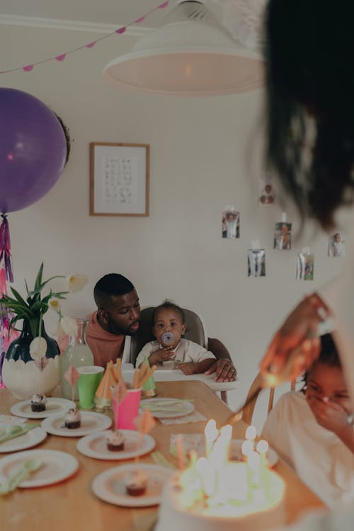 Mother Lighting Candles on the Birthday Cake and Father with Children Sitting at the Table 