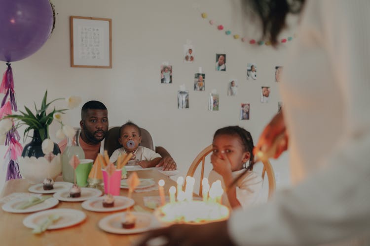 Mother Lighting Candles On The Birthday Cake And Father With Children Sitting At The Table 