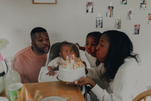 A joyful family celebrating a baby's first birthday with cake and candles indoors.