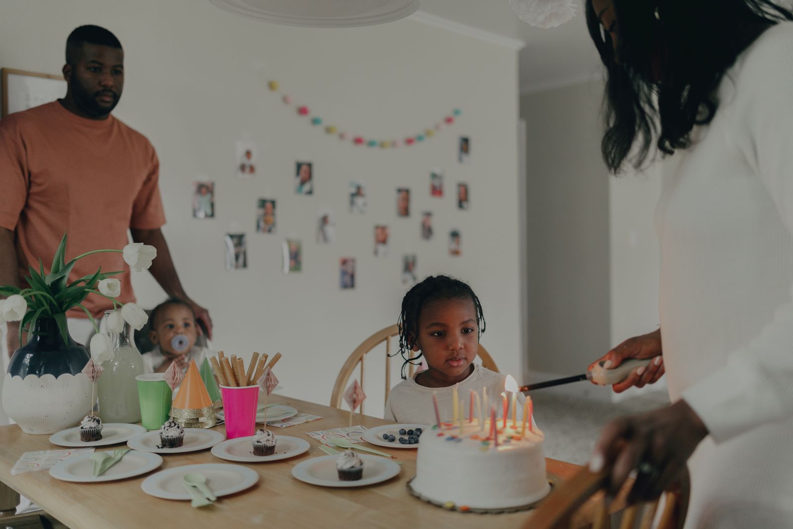 Adults and children sit around a decorated table with a birthday cake and candles.
