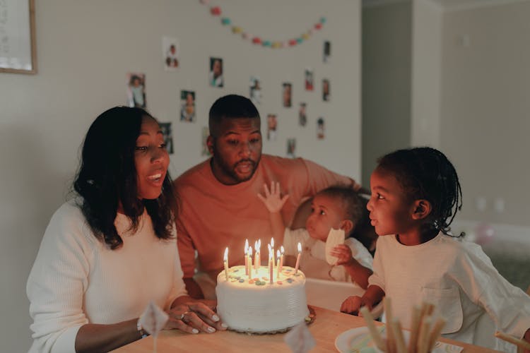 A Family Sitting Near A Birthday Cake With Lit Candles