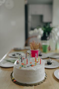 White frosted birthday cake with candles on a decorated table, ideal for celebration themes.