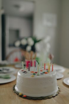 Celebratory white cake with colorful candles on a decorated table indoors.