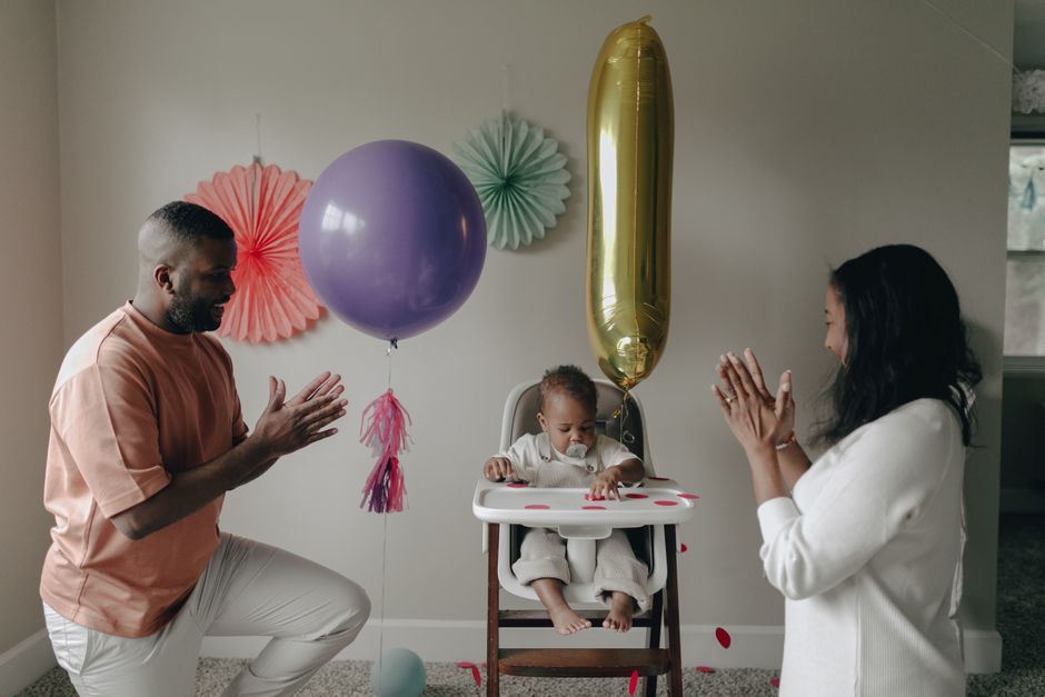 A joyful family celebrating a baby's birthday with colorful balloons indoors.