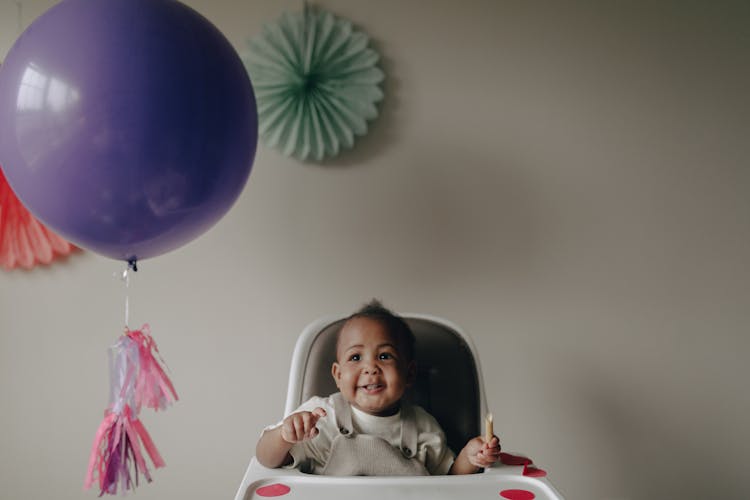 Baby Sitting On High Chair While Looking At The Balloon