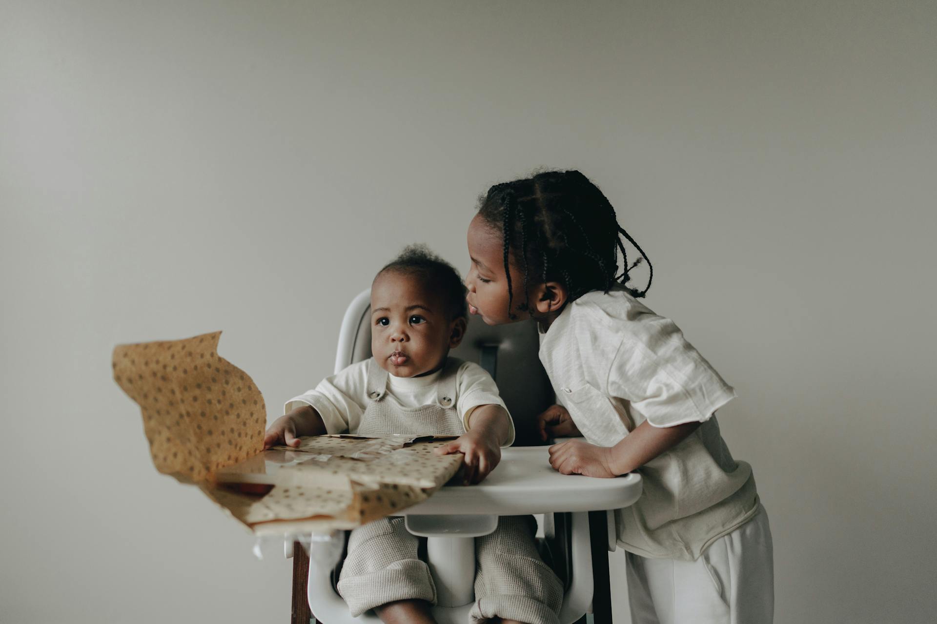 A tender moment between siblings as they explore a gift together indoors.