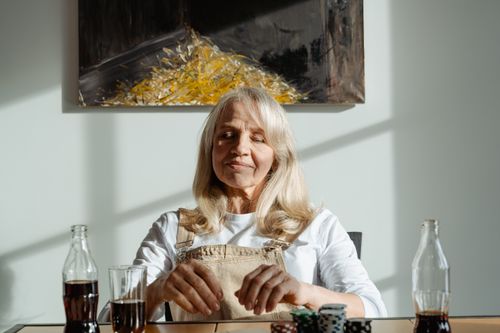 Free A happy senior woman playing poker indoors with drinks on the table. Stock Photo
