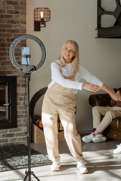 Free Joyful elderly woman dances in a cozy living room, streamed via smartphone. Stock Photo