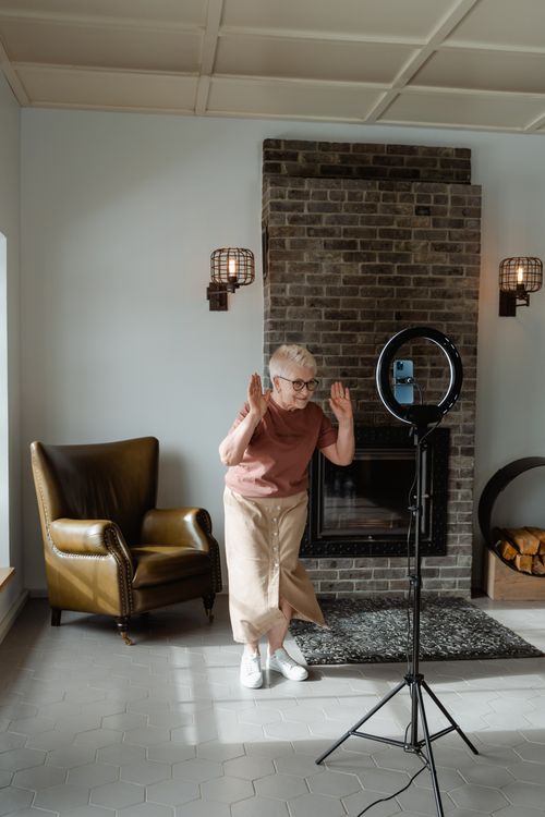 Free Joyful senior woman dancing indoors next to a camera setup in a cozy living room. Stock Photo