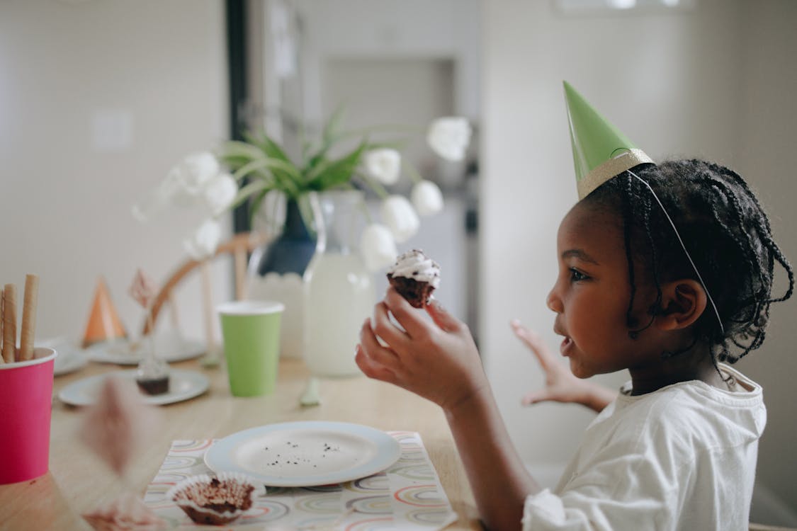 Child Wearing Party Hat Holding a Cupcake