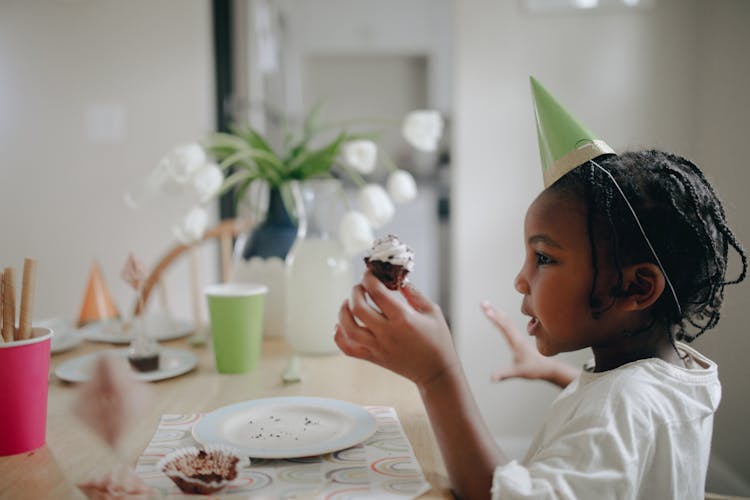 Child Wearing Party Hat Holding A Cupcake