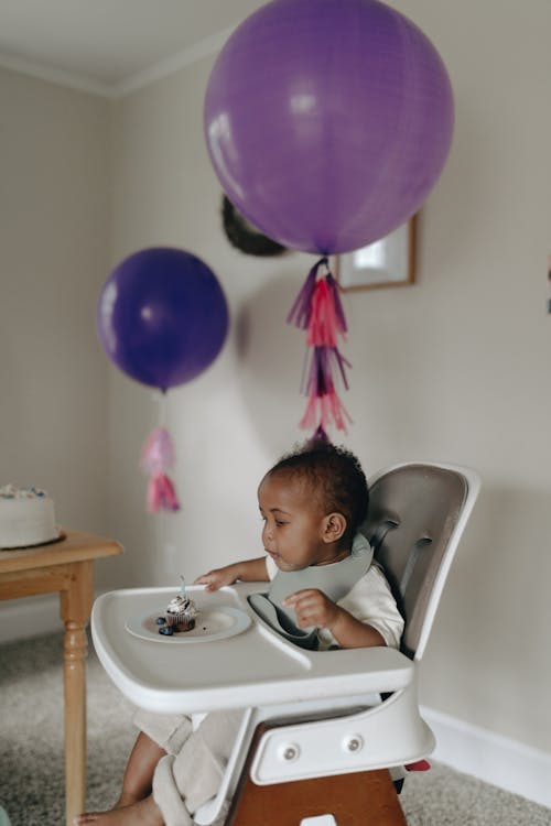 Младенец сидит на стульчике рядом с воздушными шарами