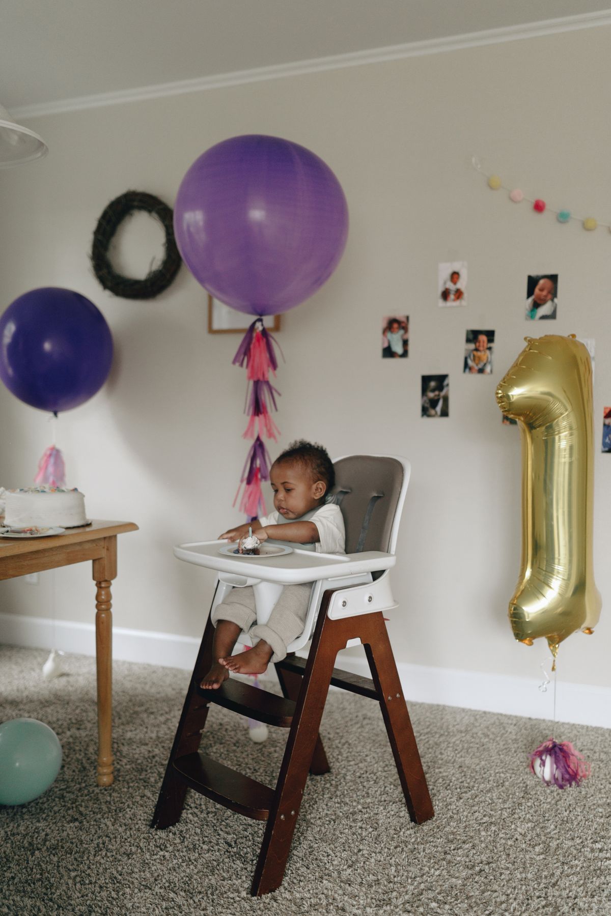 Adorable baby in high chair celebrating first birthday with balloons and cake. Stock Photo.