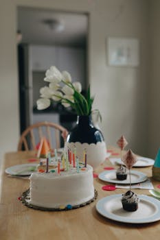 Birthday cake with candles on a table with decorations and a vase of flowers.