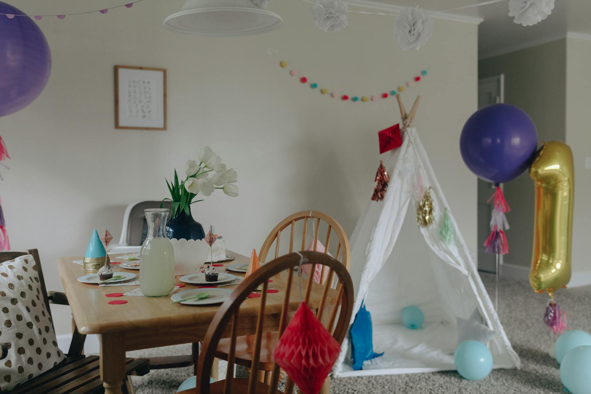 Charming first birthday party setup with balloons and a tipi indoors.