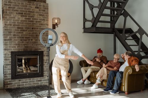 Free Elderly woman dances near smartphone while seniors relax on sofa indoors. Stock Photo