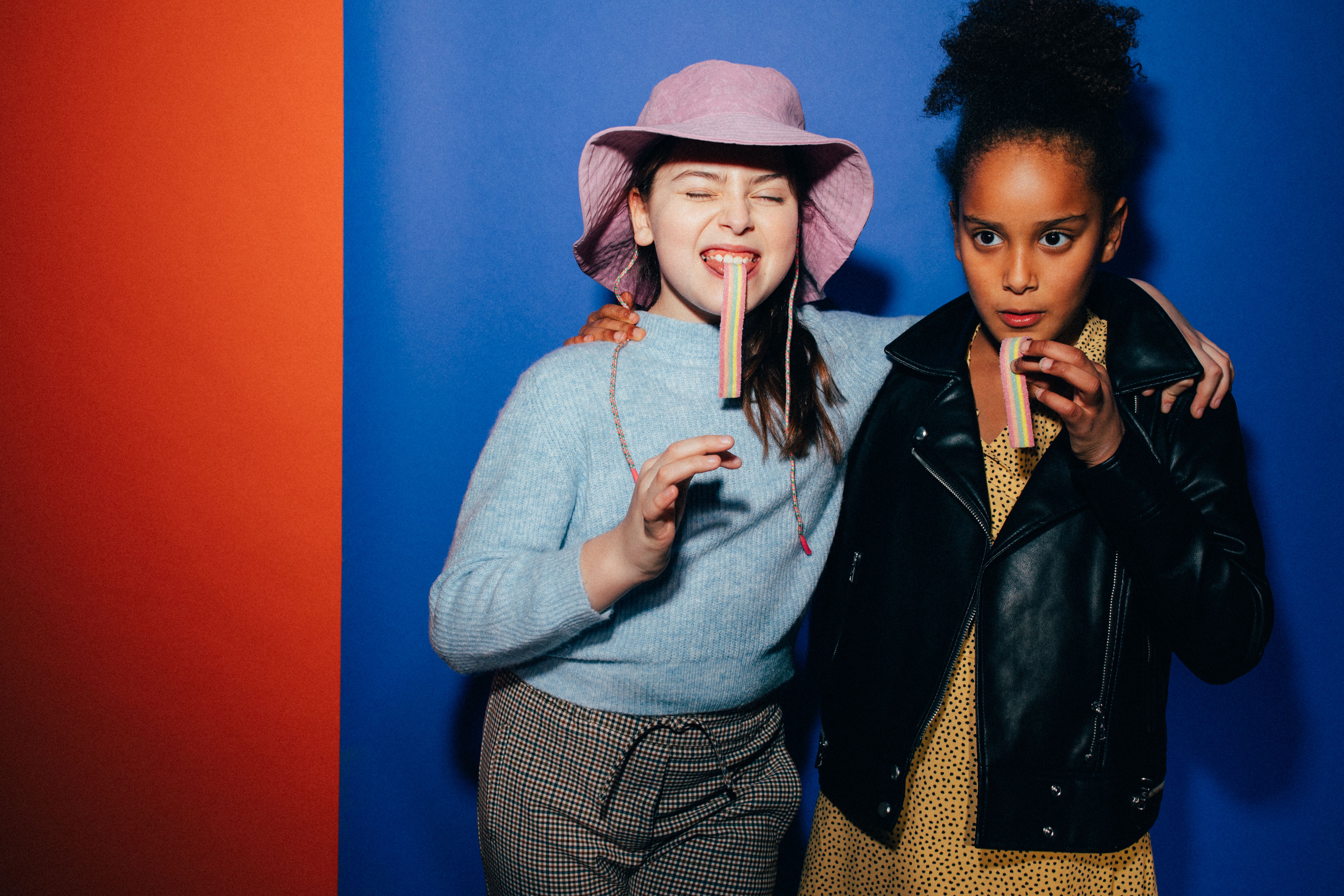 Two stylish teenage girls having fun with candy against a vibrant background.
