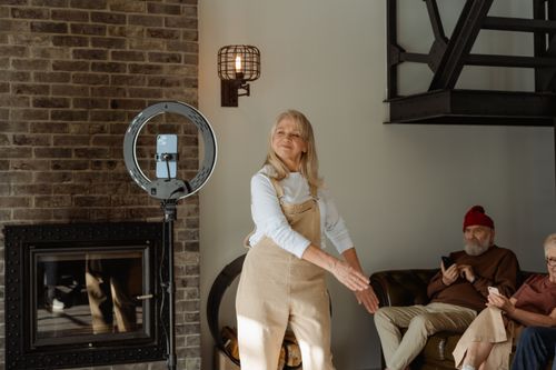 Free Cheerful senior woman dancing by a fireplace indoors, accompanied by friends. Stock Photo