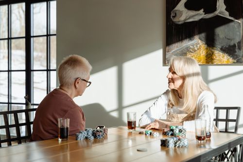 Free Two senior women sitting at a table playing poker with drinks, enjoying leisure time indoors. Stock Photo