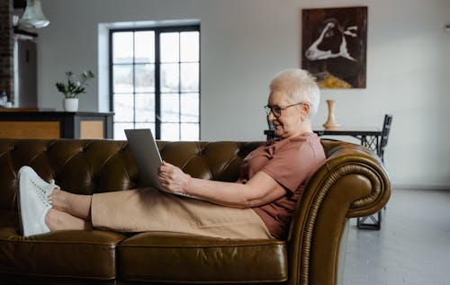 Woman Sitting on a Leather Couch Using a Laptop