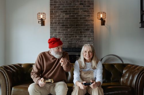 Free Happy elderly couple playing video games together on a couch indoors. Stock Photo