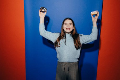 Free A smiling girl happily holds donuts against a colorful backdrop, expressing fun and joy. Stock Photo