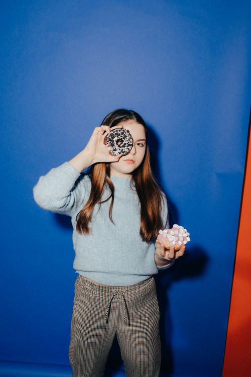 Free Child holding donuts playfully, one in front of her eye, against a vibrant blue backdrop. Stock Photo