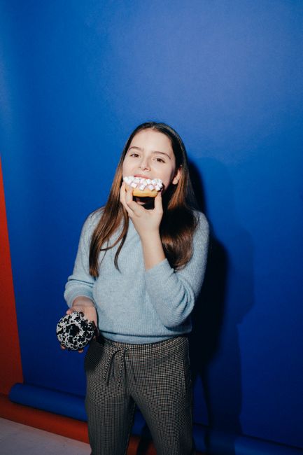 Young girl having fun eating colorful donuts against a vibrant blue background.