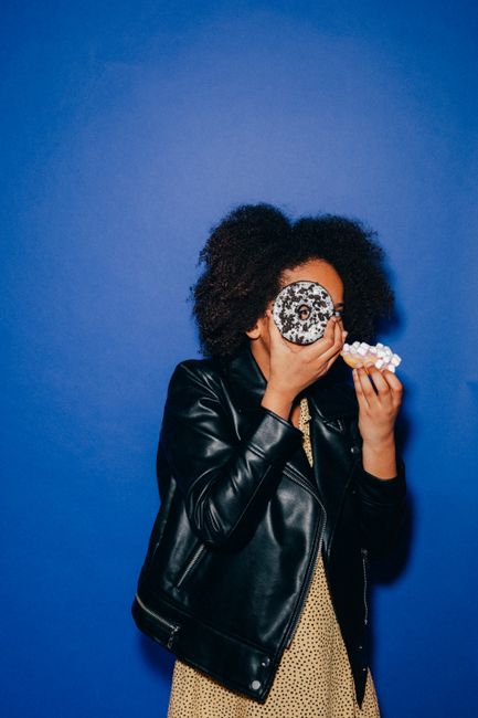 Fun photo of a girl with afro hairstyle enjoying donuts against a vibrant blue backdrop.