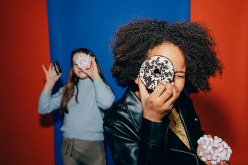 Free Two diverse kids having fun with donuts against colorful background. Stock Photo