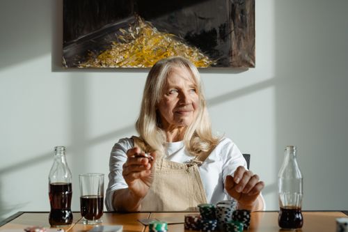 Free Senior woman enjoying a poker game and a drink in a sunlit room. Stock Photo