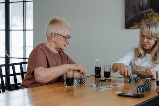 Two senior women enjoying a game of poker at a table indoors, surrounded by poker chips and cards.