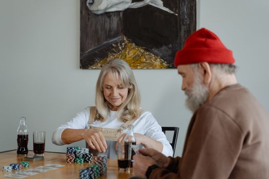 Senior couple playing cards with poker chips, enjoying leisure time indoors