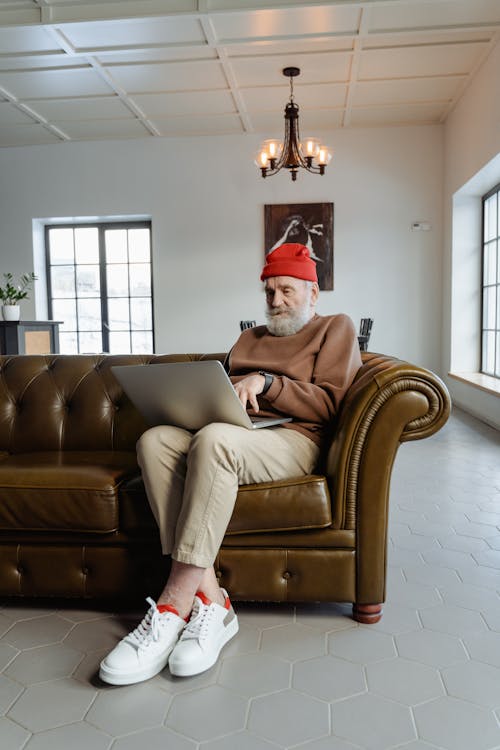 Man in Brown Sweater Sitting on Brown Leather Sofa Chair Using a Laptop