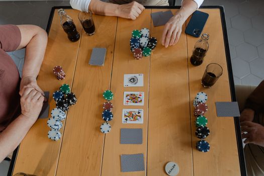 A group of friends playing poker with cards and chips on a wooden table indoors.