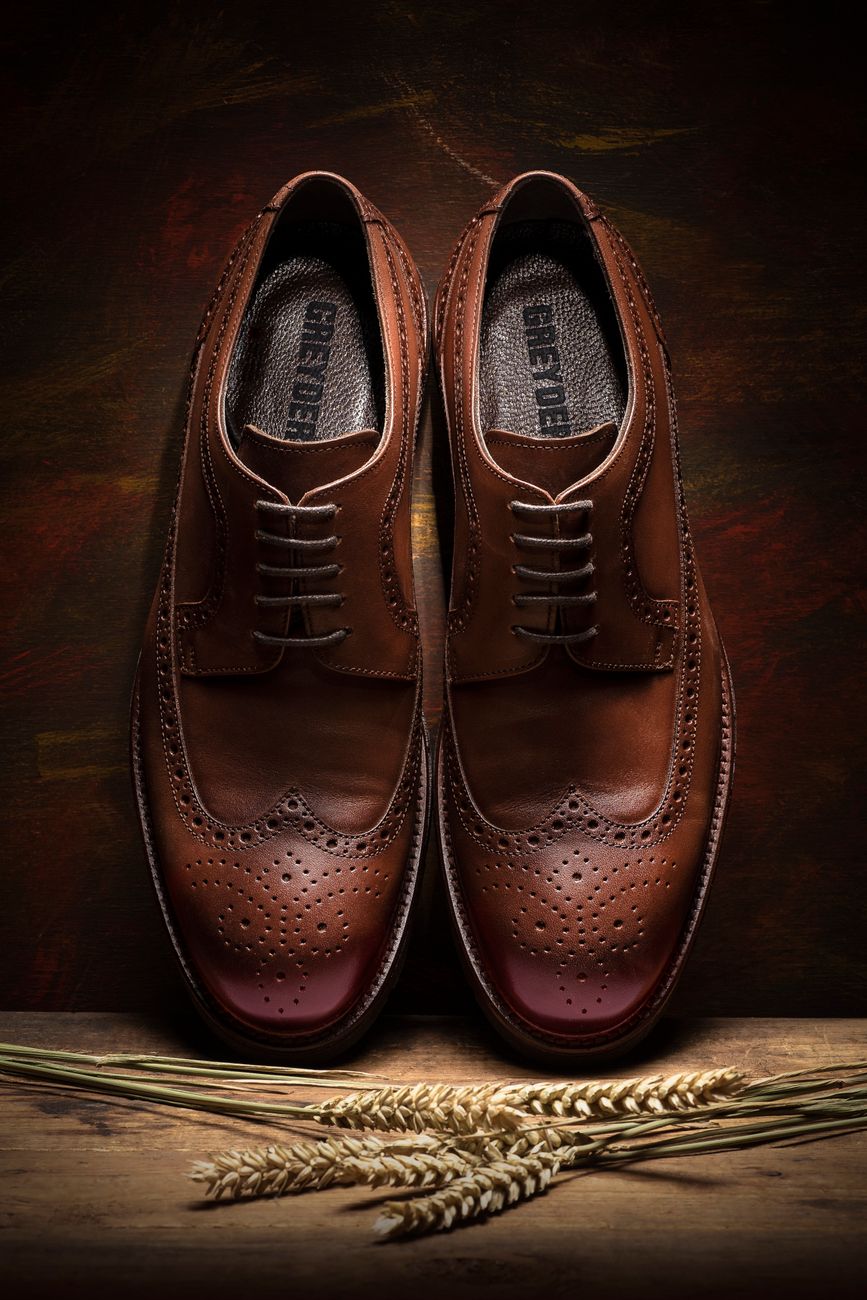 Close-up of stylish brown leather brogue shoes with decorative wingtips displayed with wheat stalks.