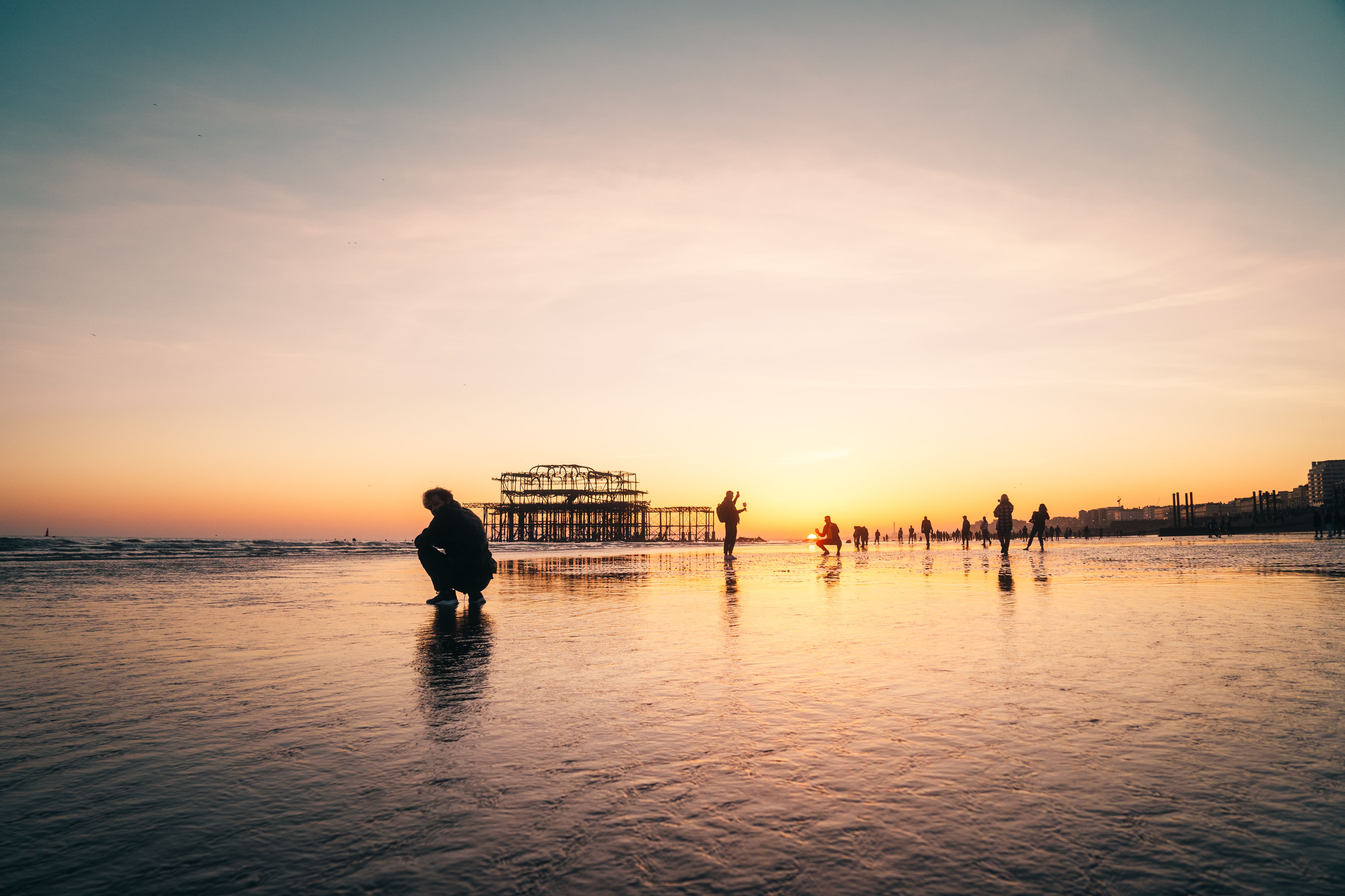 Silhouettes on Brighton Beach at sunset with the iconic West Pier in the background.