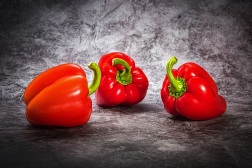 Free Three red bell peppers displayed on a textured gray background, perfect for healthy lifestyle themes. Stock Photo
