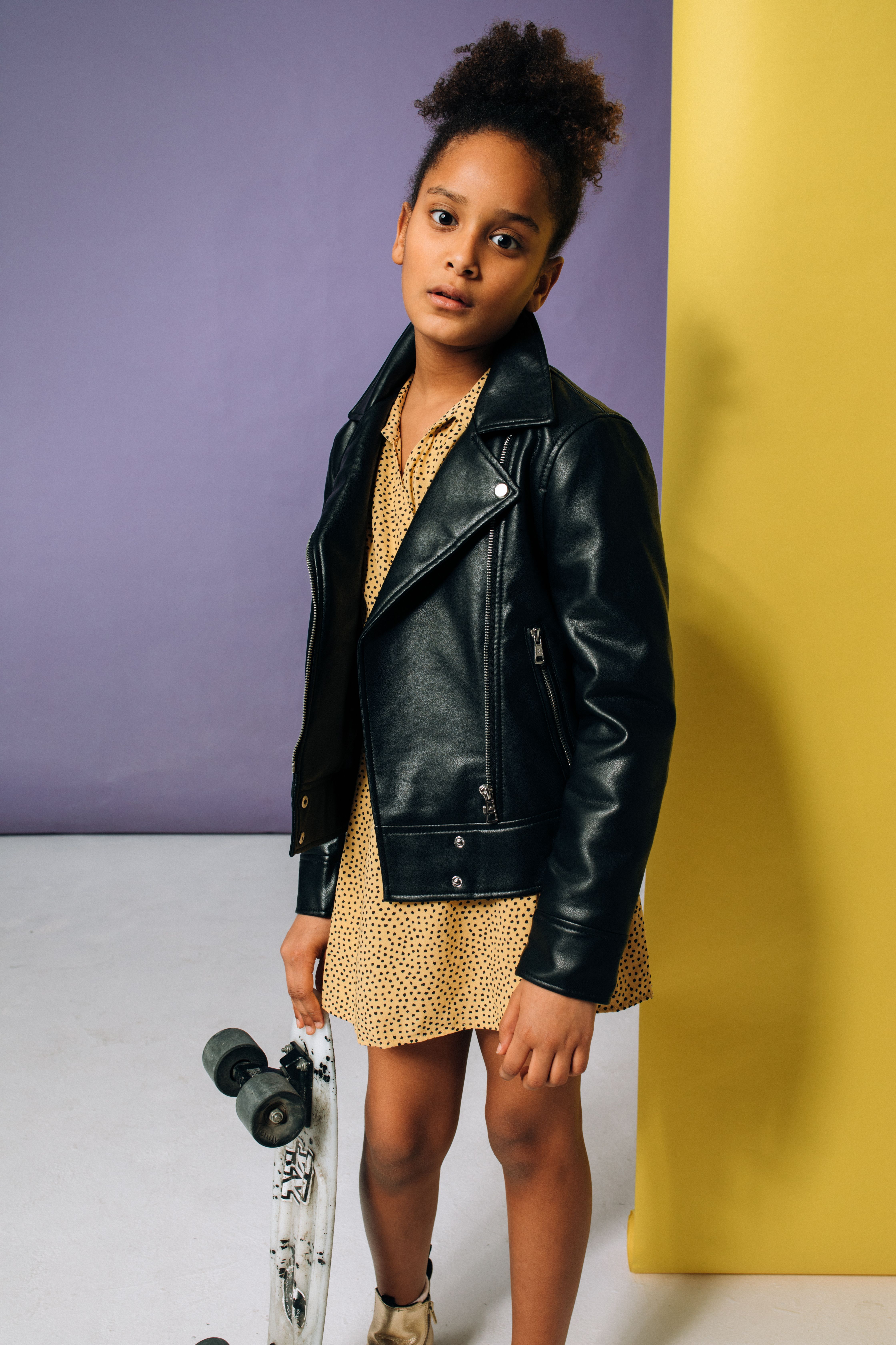 Young girl in leather jacket holding skateboard, showcasing trendy youth fashion.