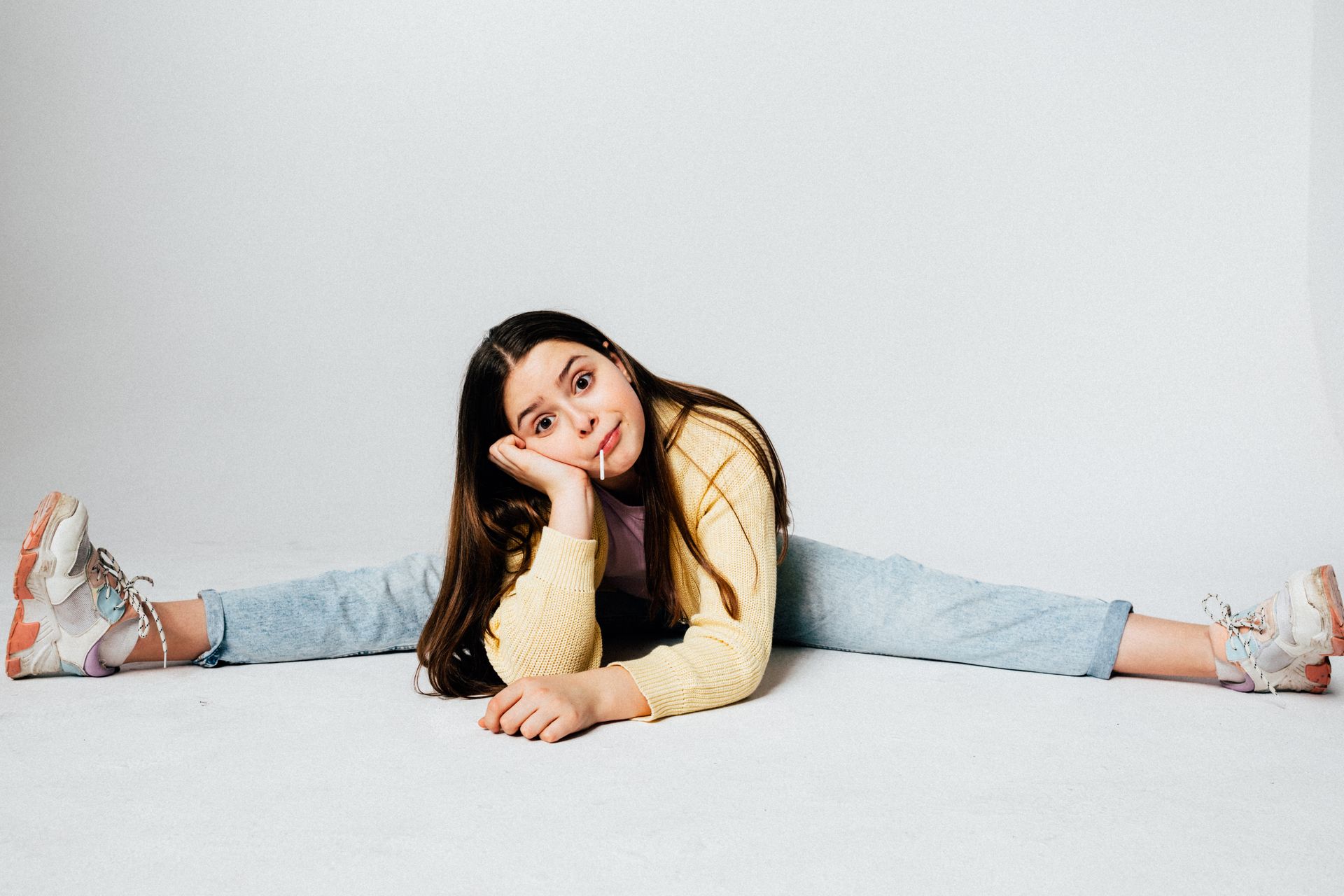 Playful young girl splits on white background, expressing joy and flexibility.