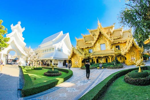 Majestic golden and white temples contrast amid lush gardens showcasing traditional Thai architecture.