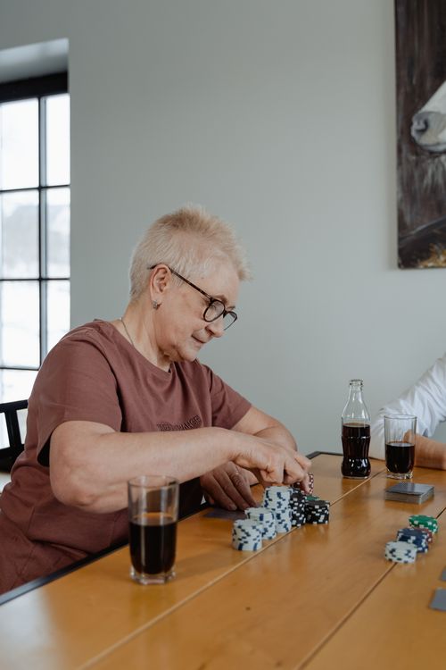 Free Senior woman enjoying a poker game at home, surrounded by drinks and chips. Stock Photo