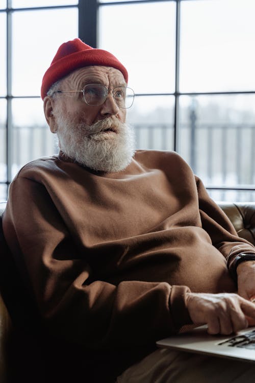 Man in Brown Sweater Wearing Red Beanie Sitting on Chair