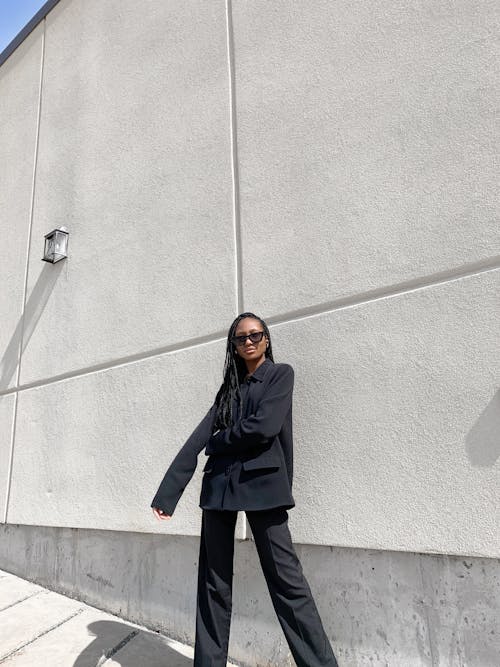 Woman Wearing Sunglasses Standing In Front of White Wall 