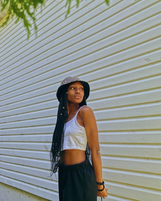 Fashionable young woman wearing a bucket hat and stylish outfit poses confidently outdoors against a textured wall.