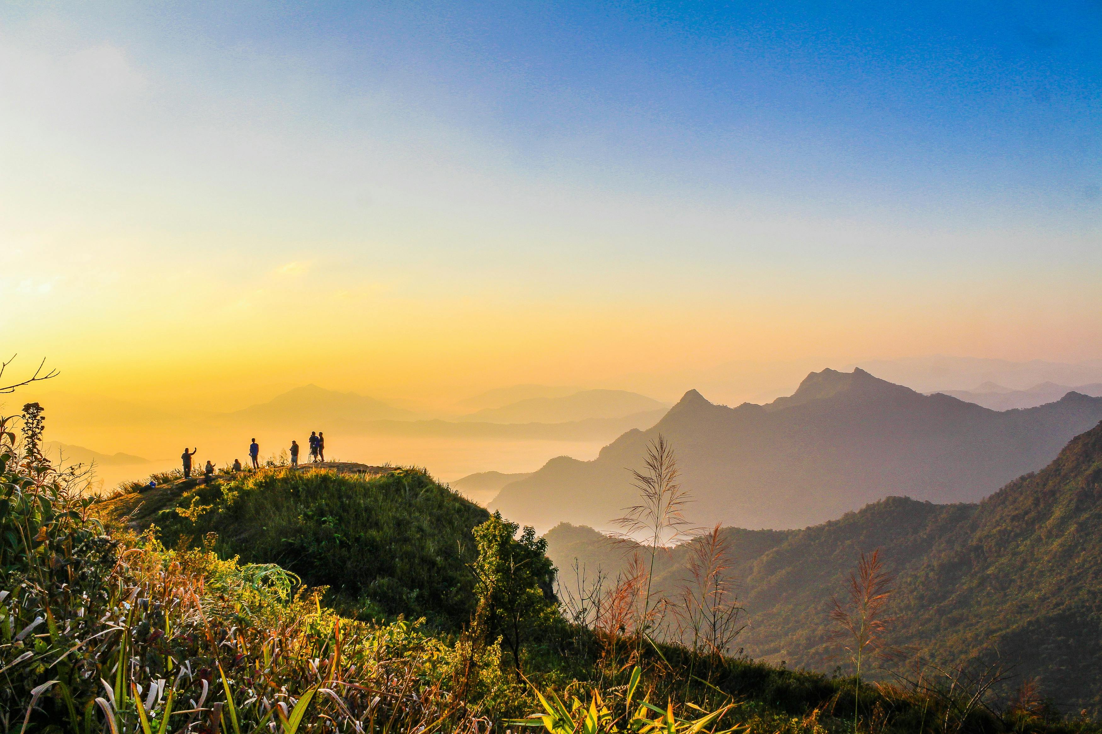 photo of people standing on top of mountain near grasses facing mountains during golden hours