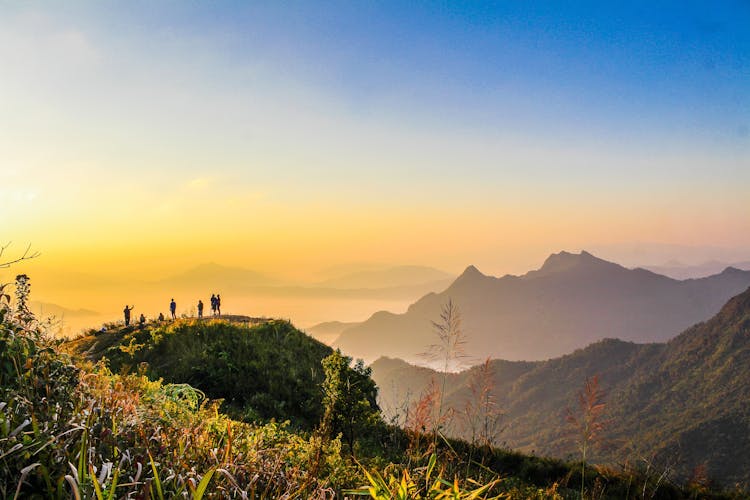 Photo Of People Standing On Top Of Mountain Near Grasses Facing Mountains During Golden Hours